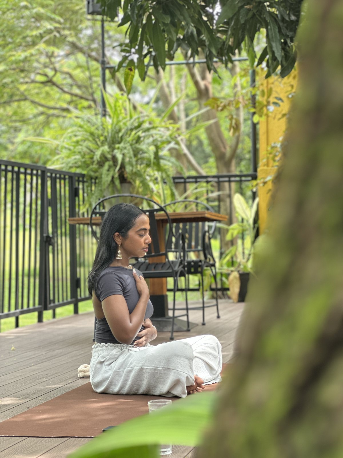 A woman seated in meditation on the leafy outdoor deck at Svastha Studio